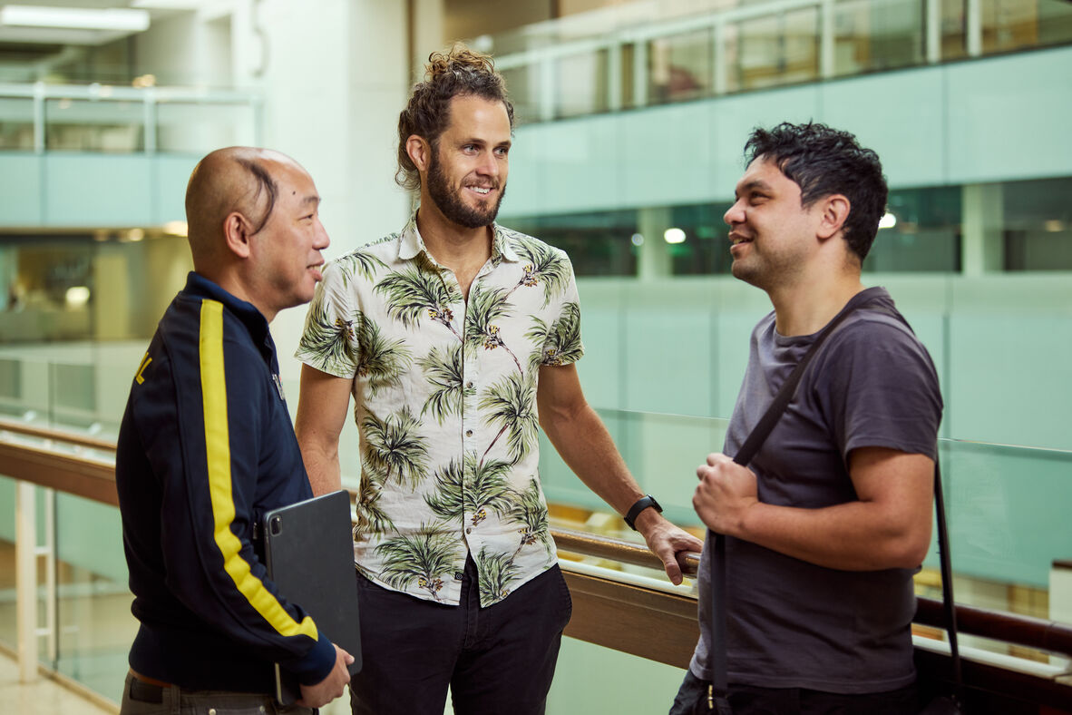 Three visitors of diverse backgrounds standing and talking together inside State Library