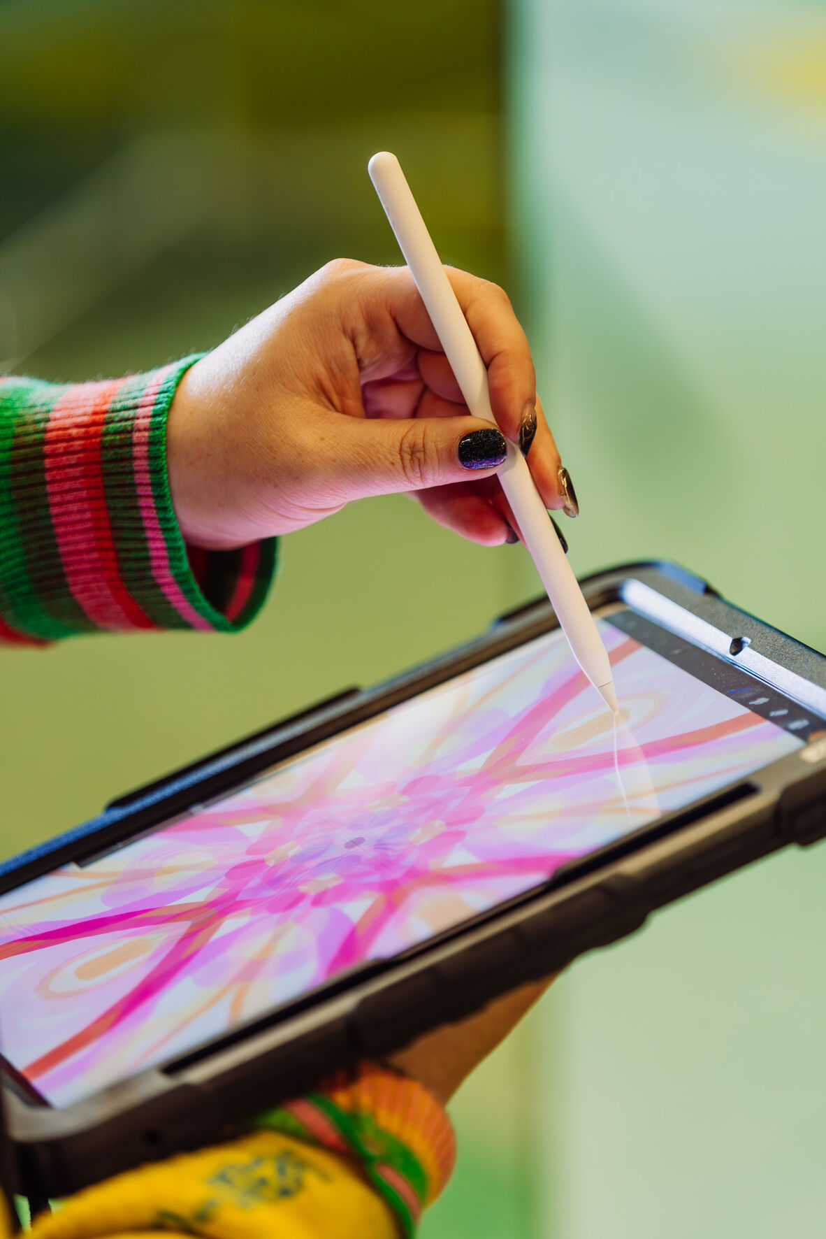iPad with a black cover being held by a person who is drawing with an apple pencil. On the ipad screen Procreate is open and there are a number of bright, colour swirls and lines.