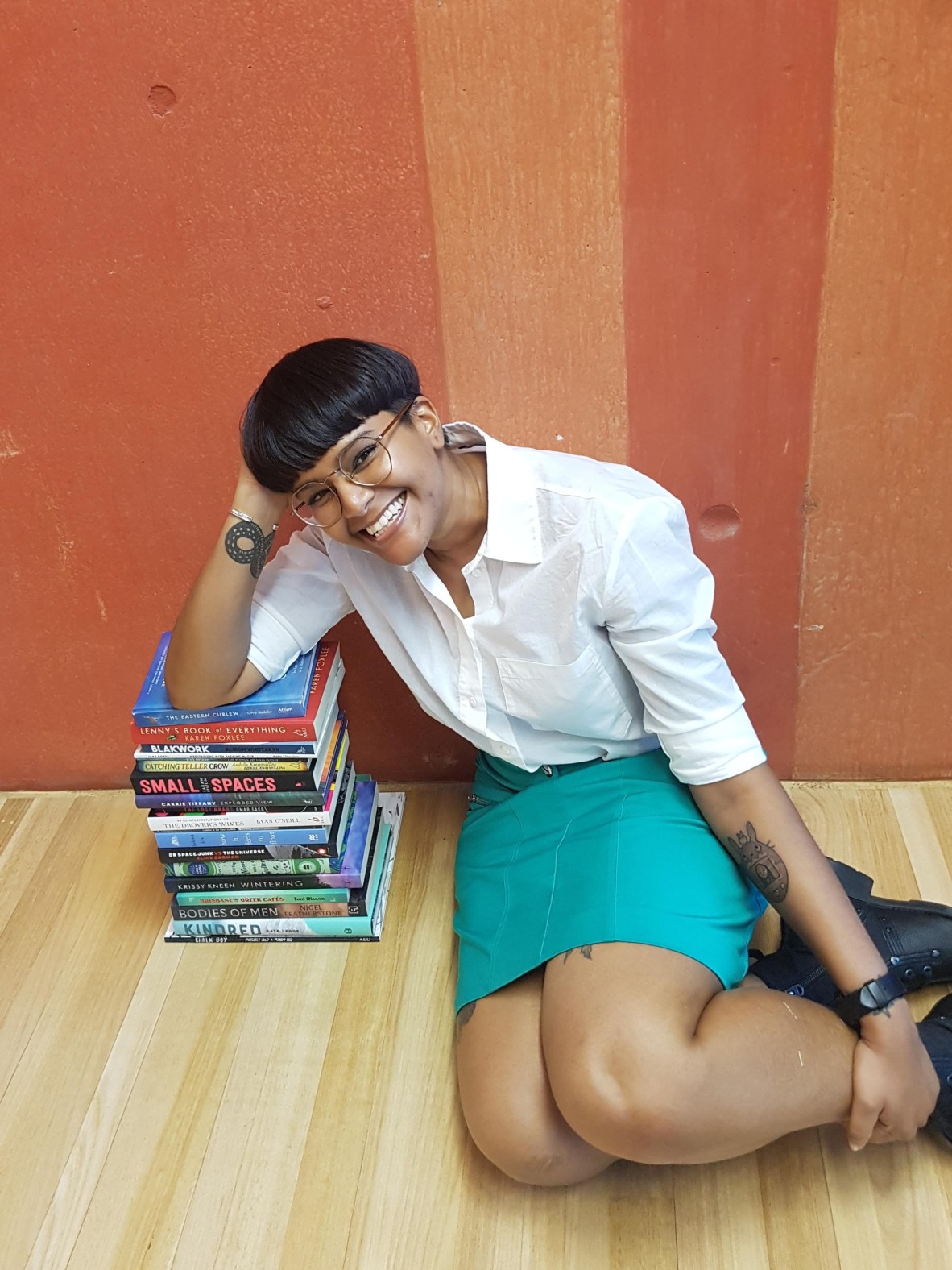 Shastra Deo sitting on a wood floor leaning her elbow against a stack of books