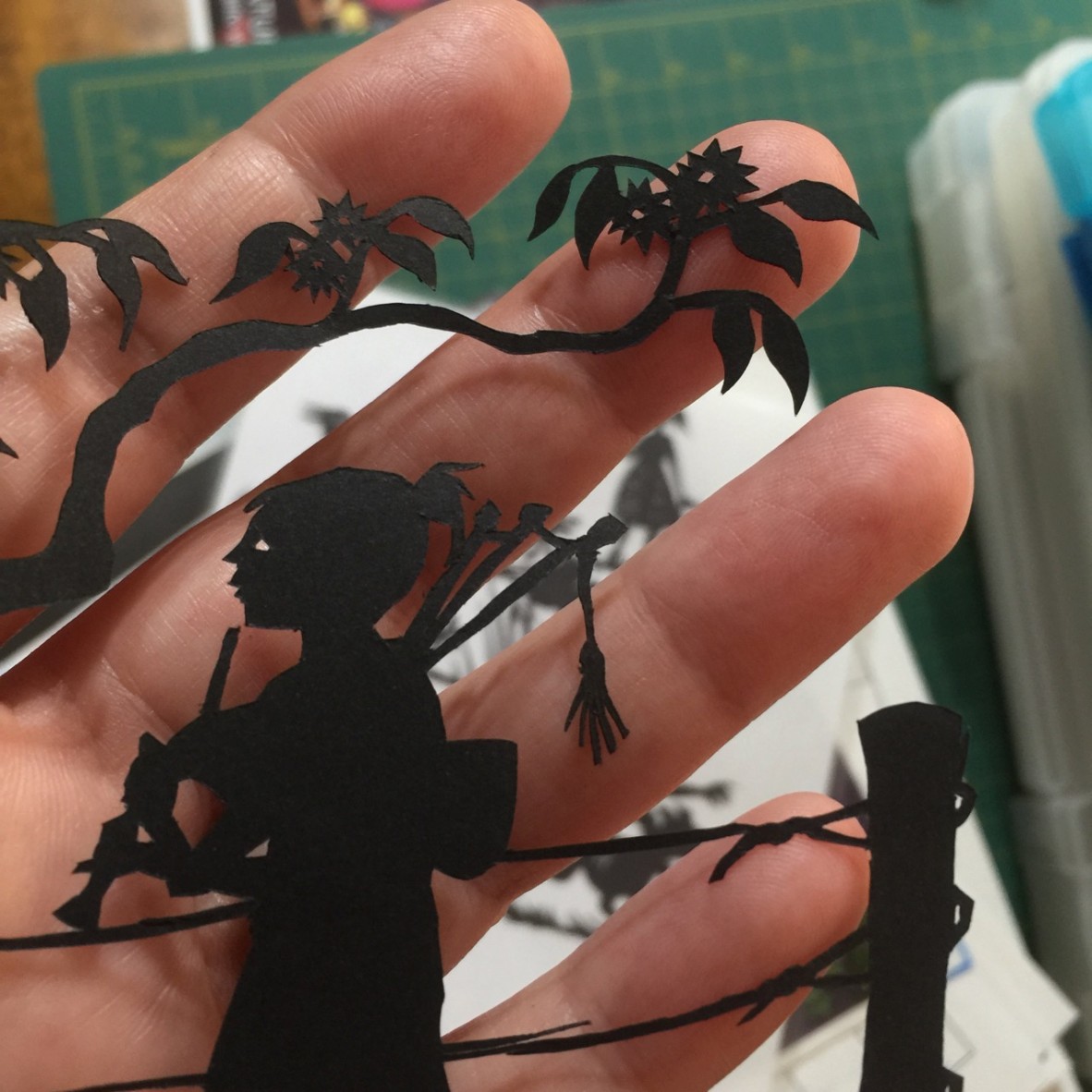 A hand holding a black paper cut-out of a figure playing bagpipes