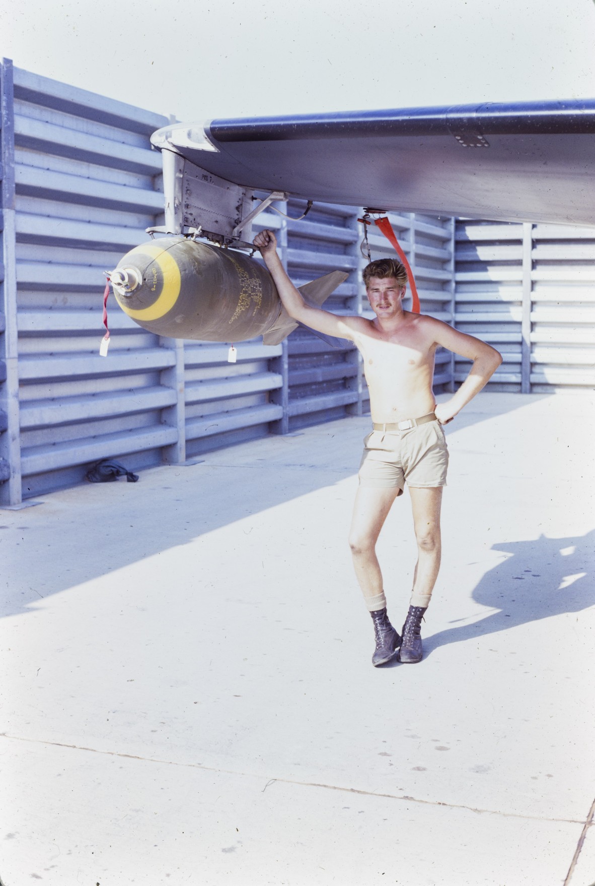 Jack Wesley, 2 Sqn Engine Fitter, leans against a mounted bomb on the wing of a Canberra Bomber.