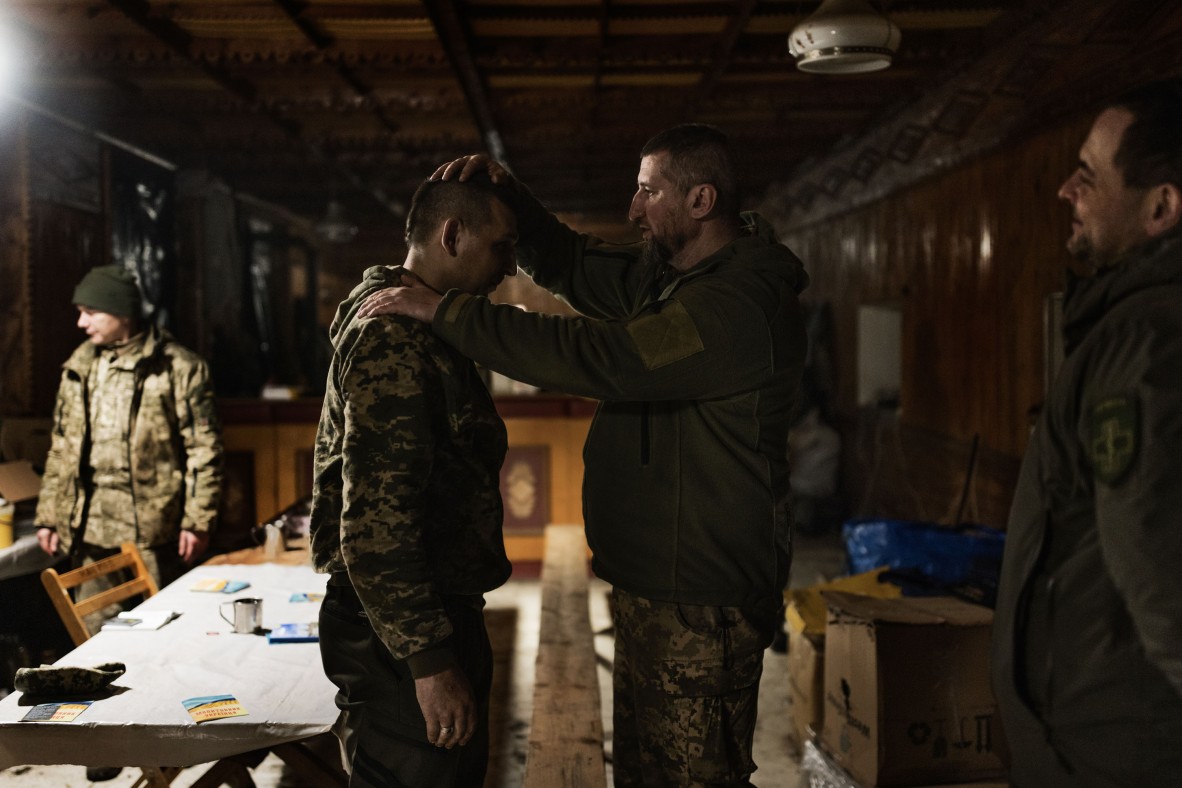 A photo of soldiers in a room with one of them blessing another man on the head