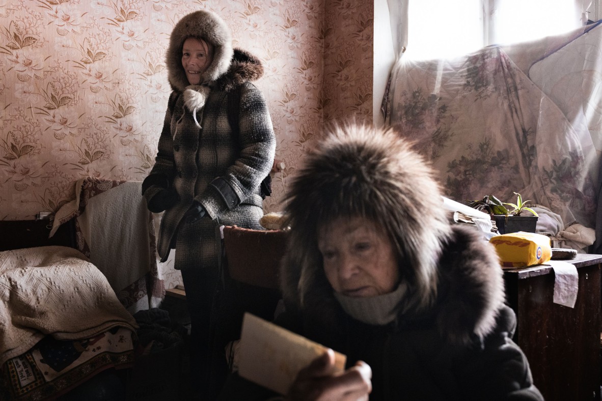 A photo of two elderly women in a room, one is looking at old photos