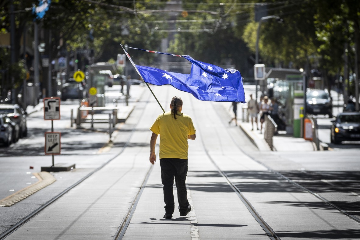 A photo of a man carrying an Australian flag with the Union Jack cut out while walking down middle of a street in Melbourne to join the Invasion Day Rally