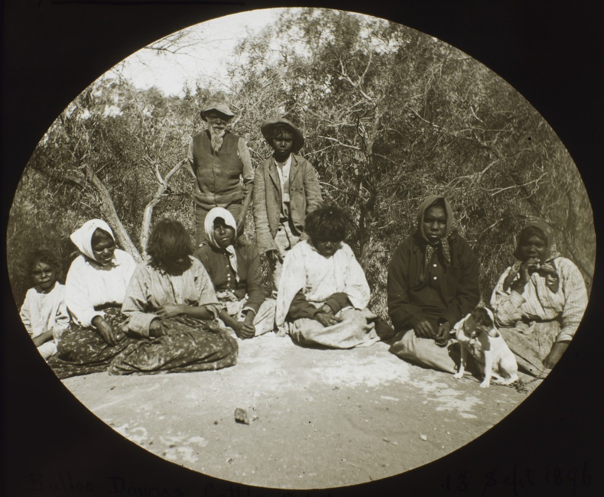 Group of First Nations peoples sitting in front on shrubs