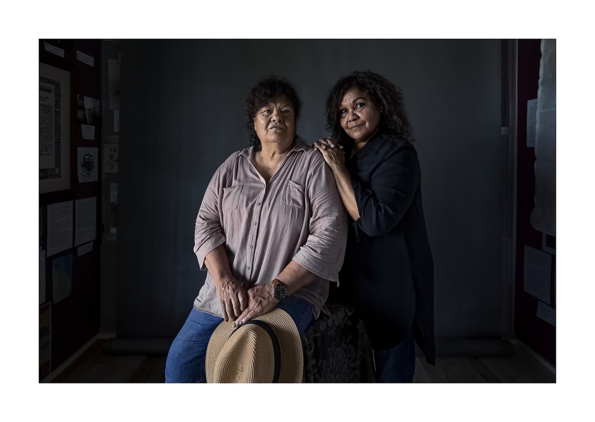 Two First Nations women against dark grey wall