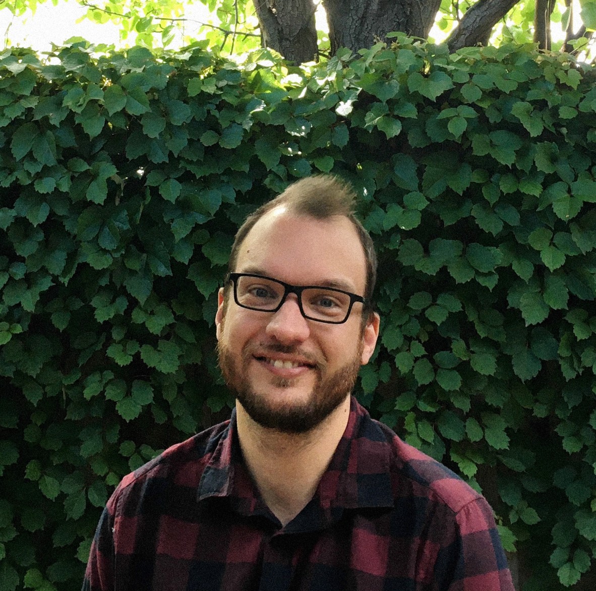 Photo of Alan Vaarwerk who wears glasses and a checkered shirt. He sits in a garden.