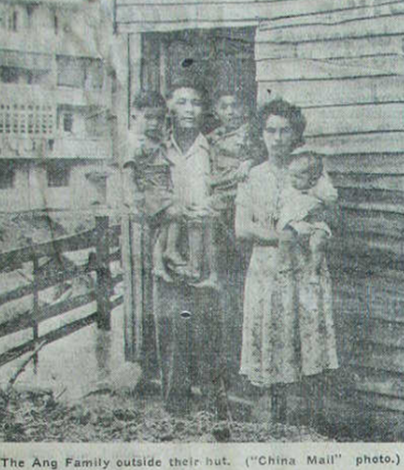 A portrait of a family, mother, father and three children outside a hut