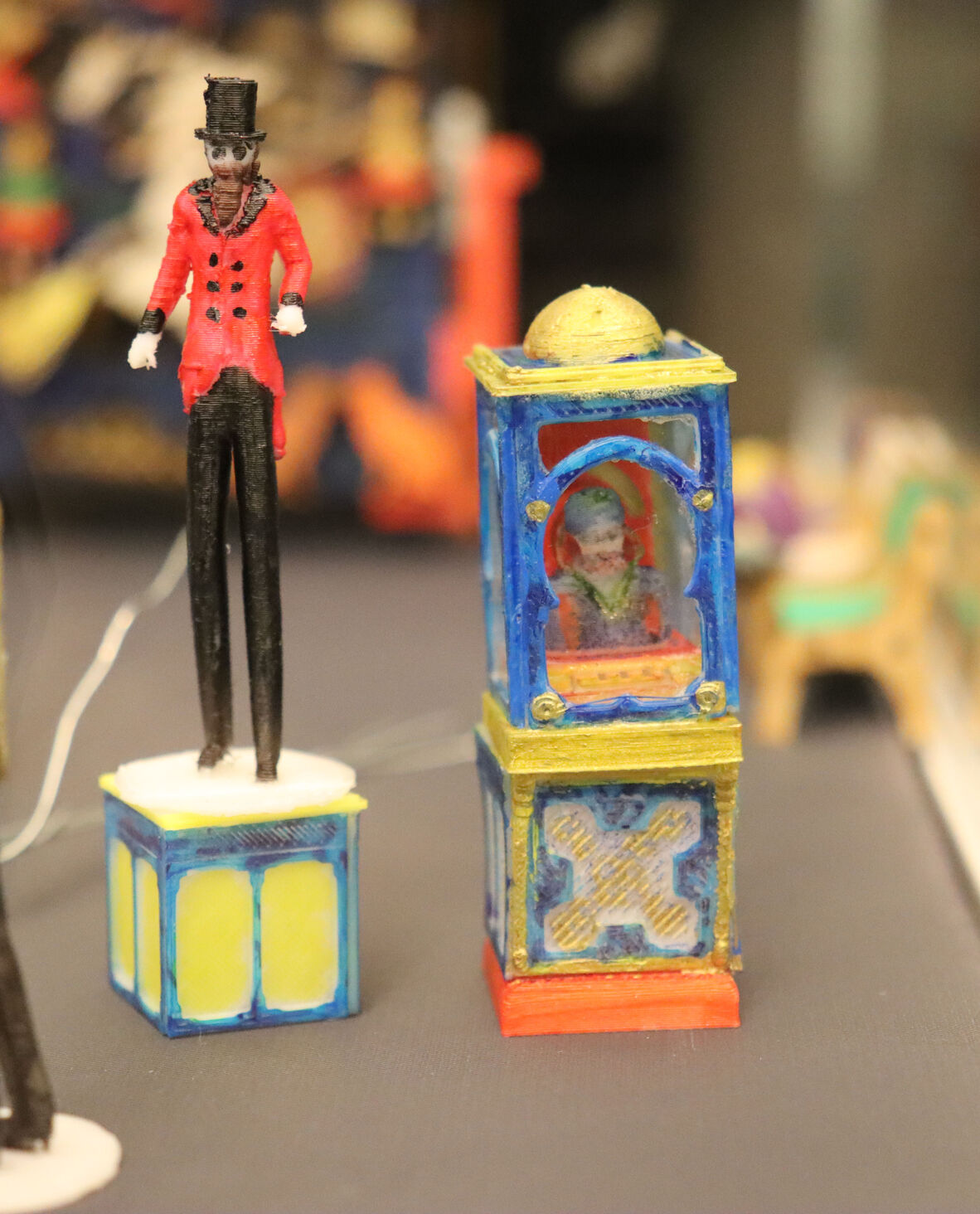 Image of a tiny Zoltar Speaks animatronic fortune telling machine and a colourful bearded clown dressed in a red and black suit, top hat wearing stilts.