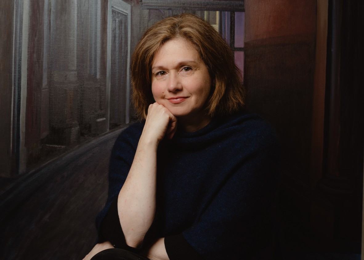 Artist Anne Wallace in dark clothing against a painted background.