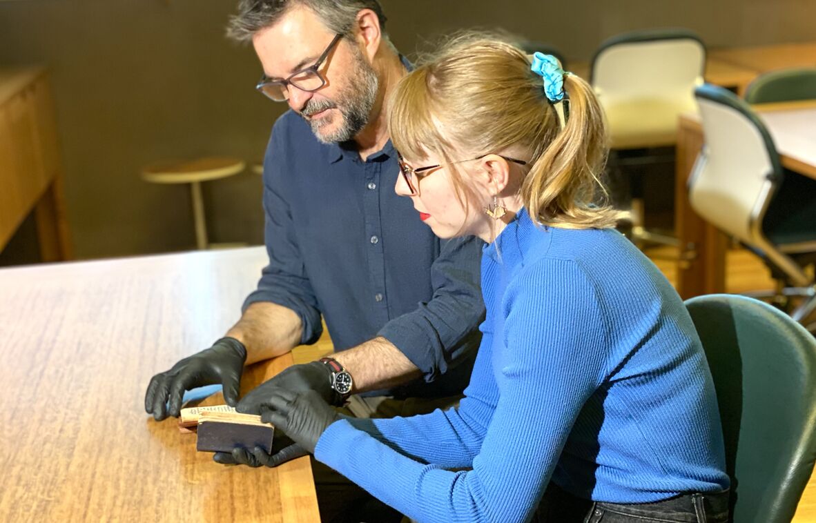 Bearded man and young woman both wearing black gloves and looking at small historic pocket diaries