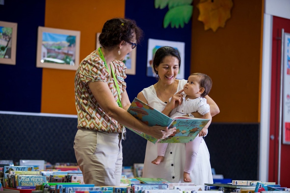 Mother and baby looking at books inside library with a librarian