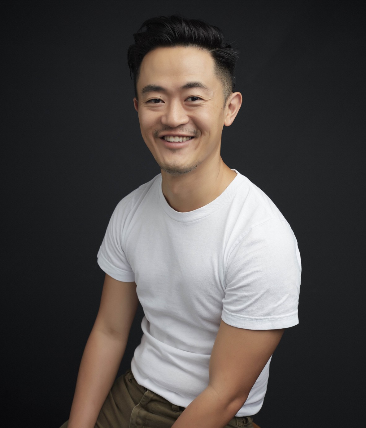 Writer Benjamin Law in a white t-shirt and jeans is seated smiling