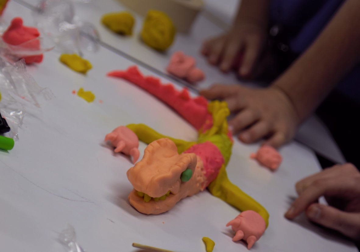 Model dragon made with plasticine and hands of children on table