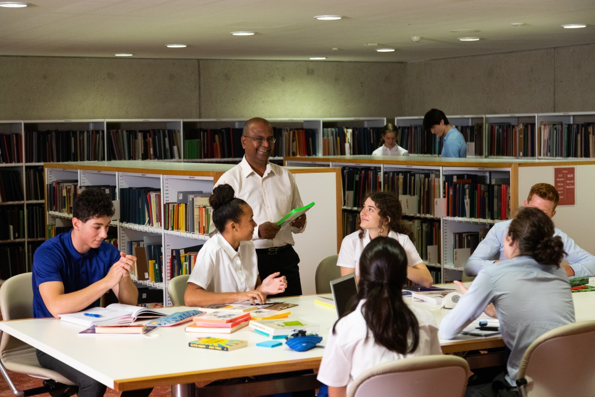 Teacher standing beside high school students seated at a desk in the State Library