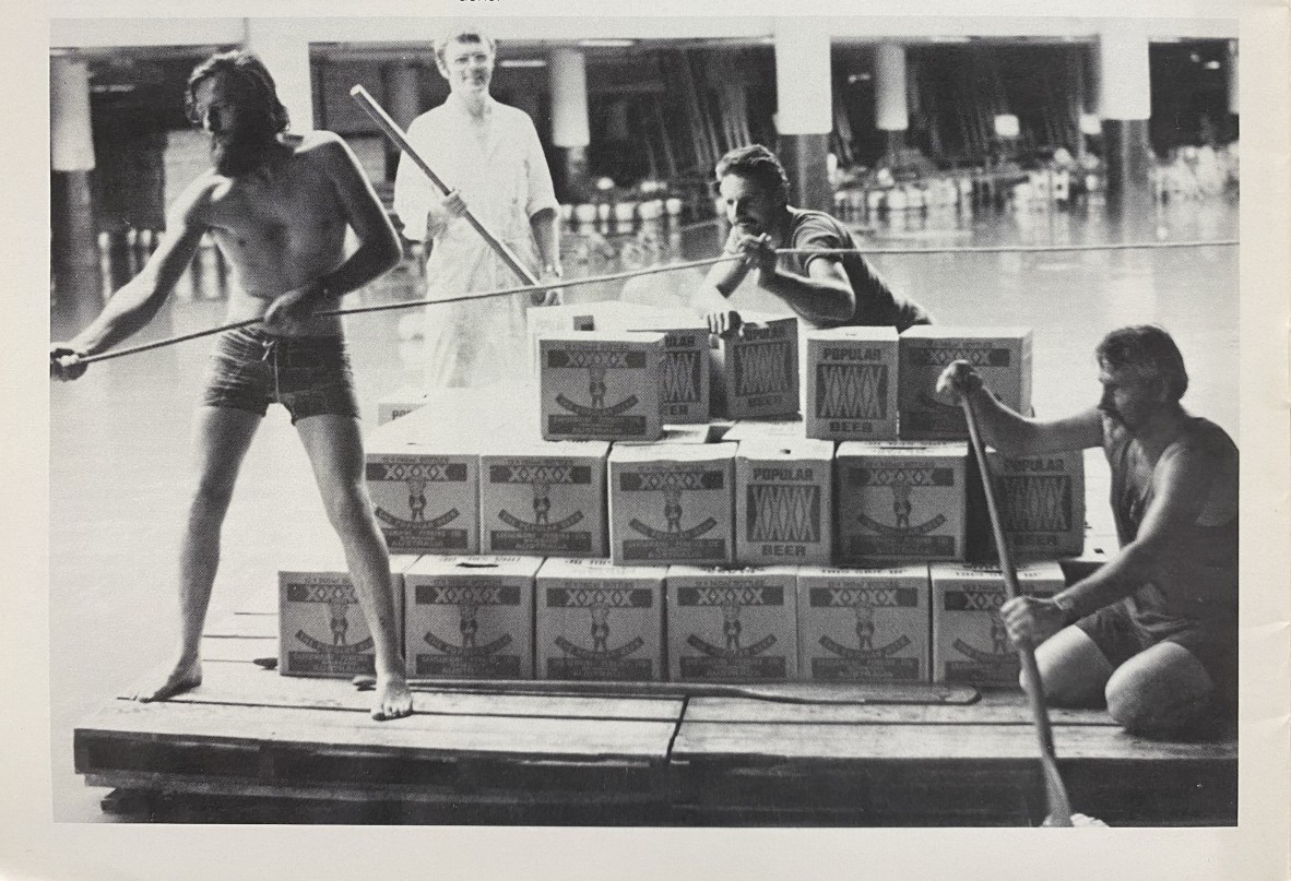 Four men on a makeshift raft ferrying beer cartons across floodwater.