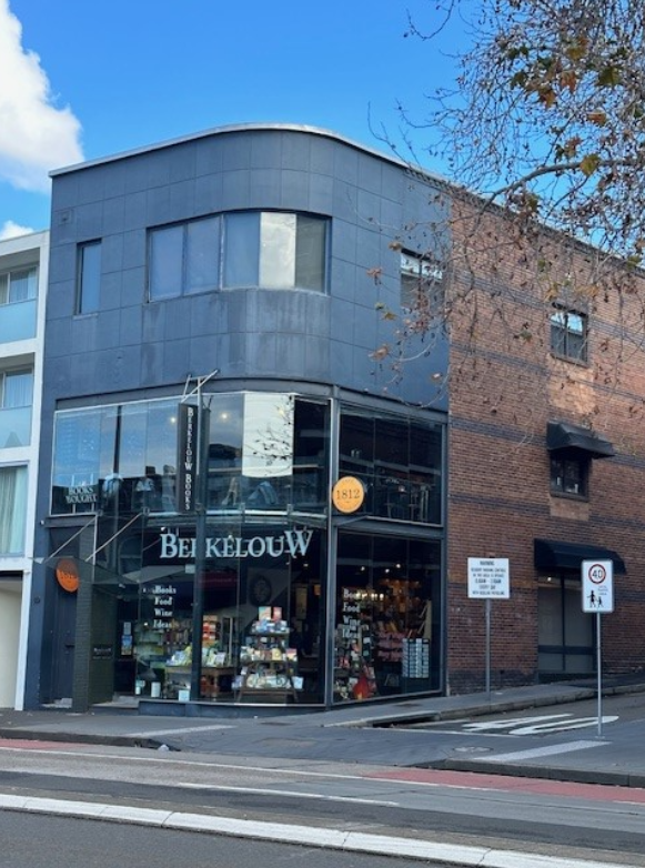 The outside of Berkelouw Books in Paddington, Sydney, showing a dark grey and glass facade and an empty street in front
