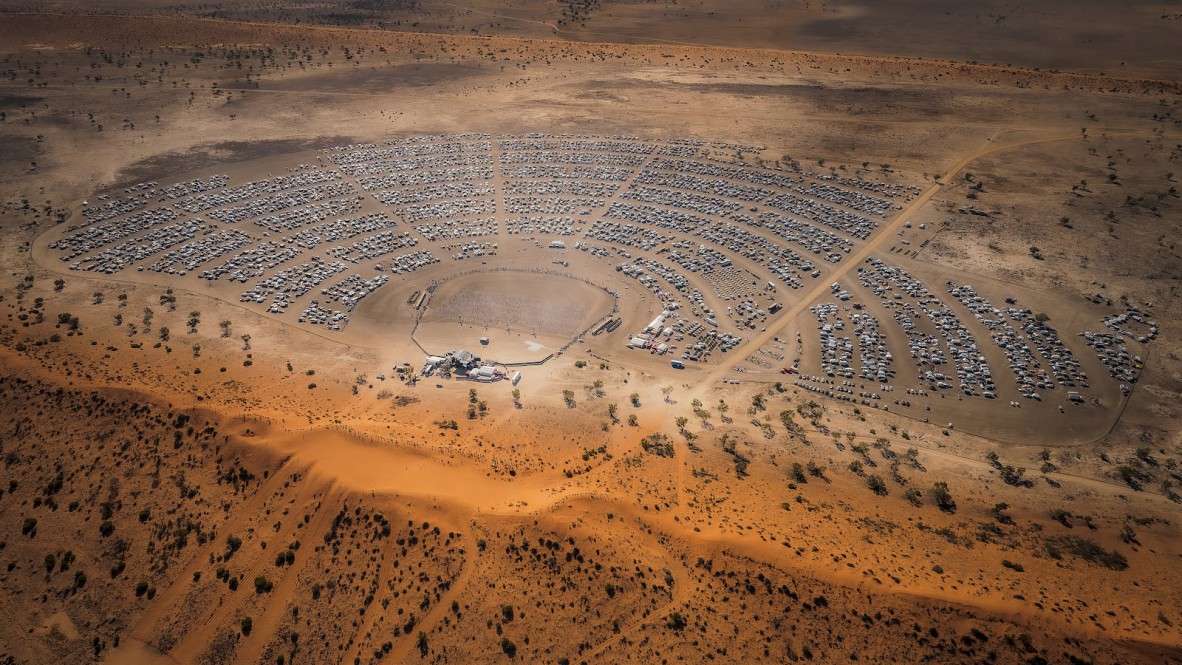 Aerial photo of desert campground on red dirt with vehicles arranged in radial pattern.