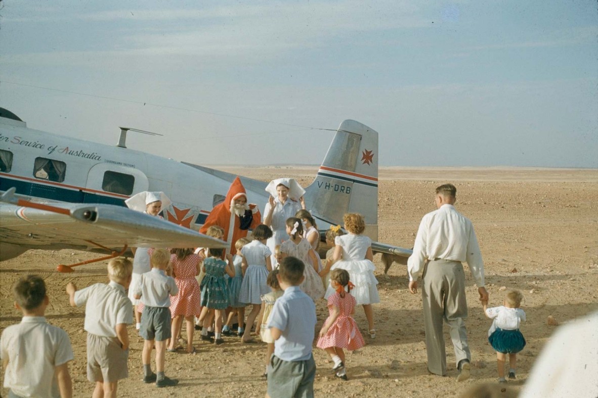 Children meet the Royal Flying Doctor plane to greet Santa Claus as part of Christmas celebrations in Birdsville, ca. 1960