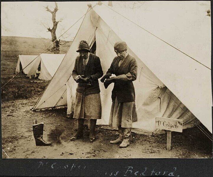 Dr Cooper and Miss Bedford cleaning boots outside a tent, Serbia.