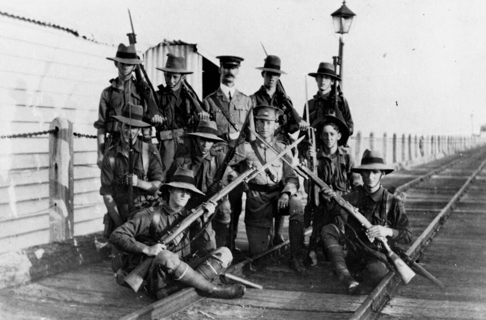 11 armed soldiers from WWI on jetty with 2 guns crossed in front of them