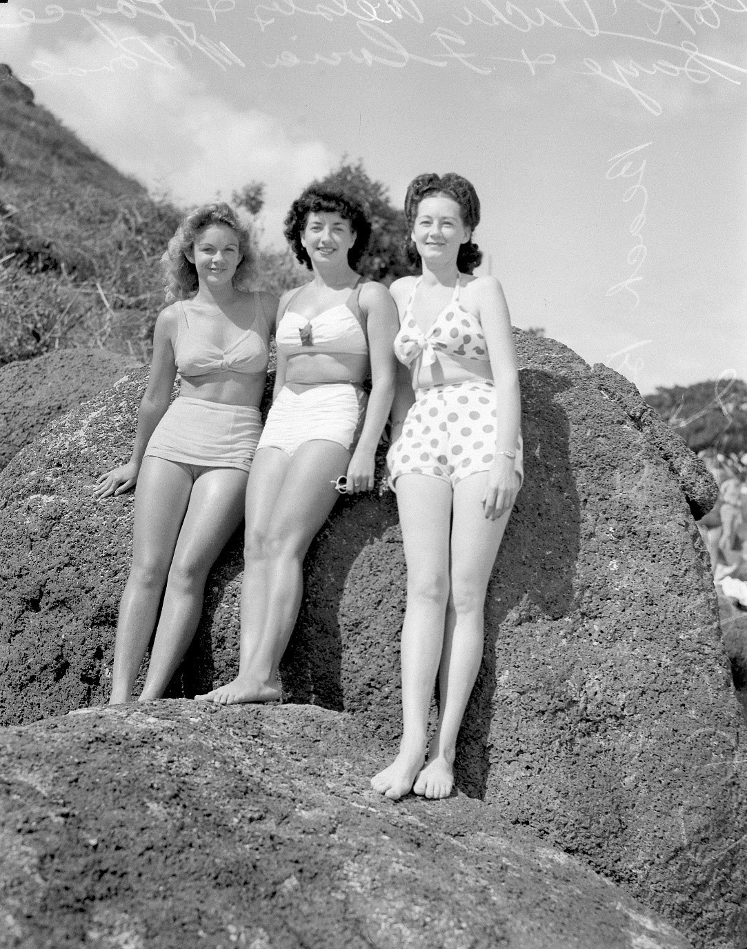 Photo of three women posing in bathing suits on rocks at Greenmount Beach in 1947