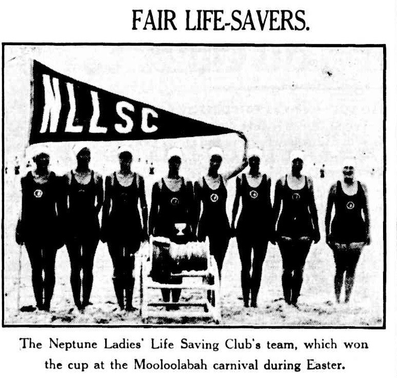 Photo of eight women life savers standing behind a life saving reel at the beach.