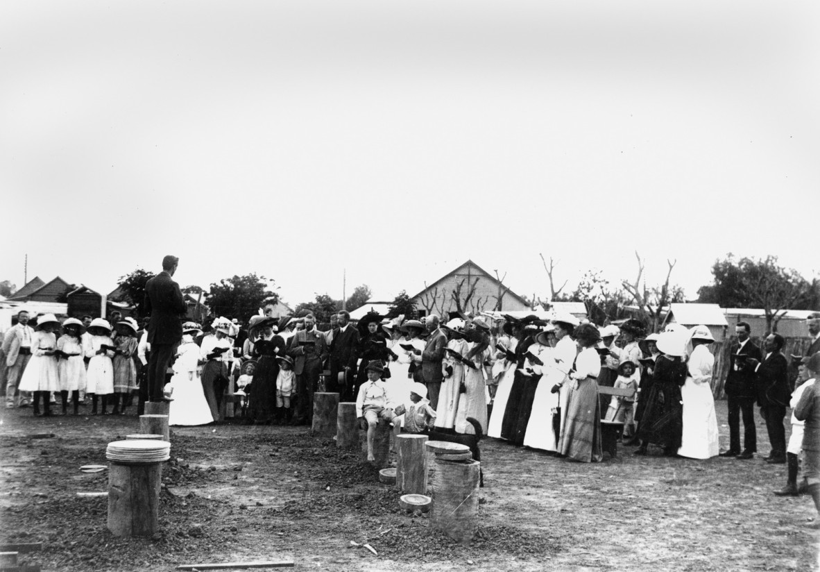 Black and white photo of a gathering of people around the stumps of a building