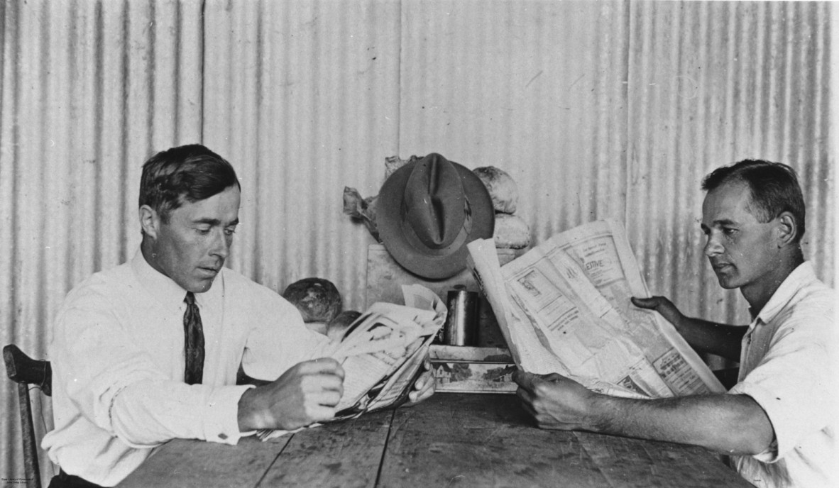 Two men sitting at a table reading newspapers ca. 1929