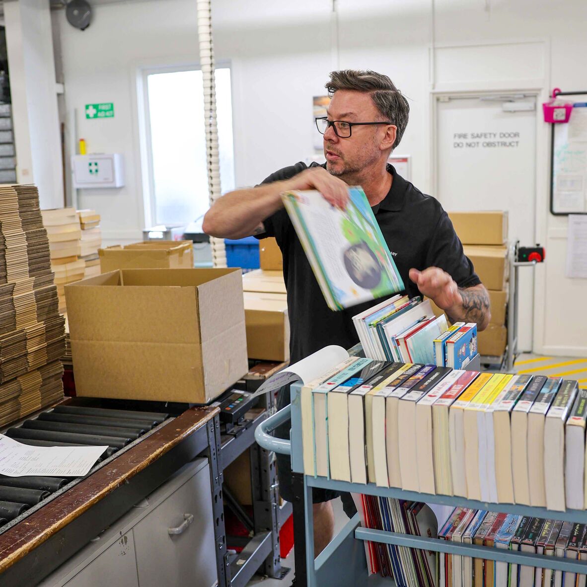Man wearing glasses packs books from trolley into box in loading dock