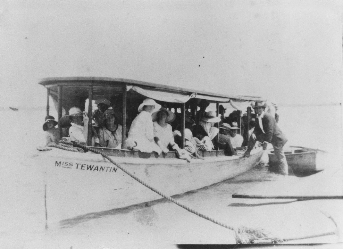 Black and white image of the vessel "Miss Tewantin" with the anchor line on the bank, while a fully-laden boatload of tourists pose for the camera, ca.1923.