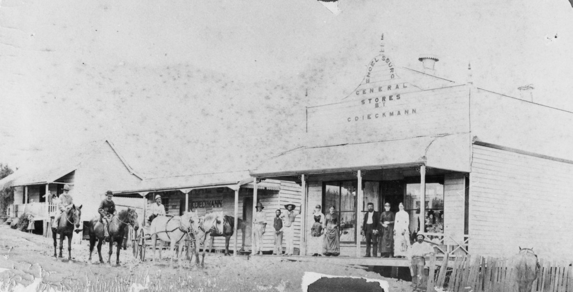 Black and white photo of store fronts at Engelsburg, now known as Kalbar, pre-1914, with men and women standing outside as well as people on horse back.