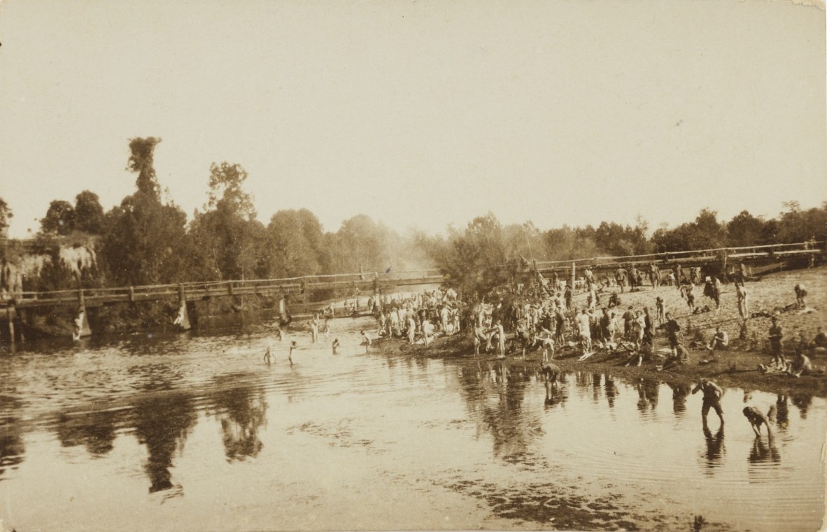 Black and white photo of the South Pine River, people on the right hand side bank, some standing in the shallow water.