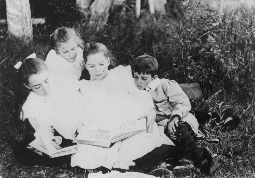 A black and white photograph of a group of children sitting on the grass reading books