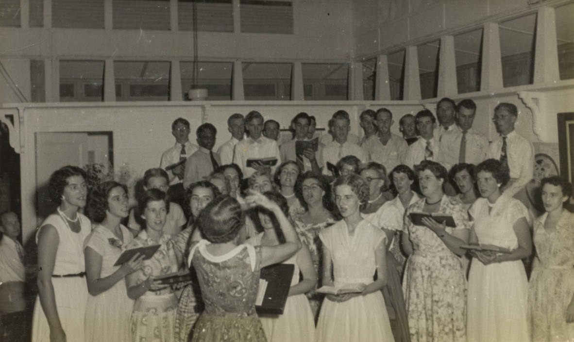 Sepia photo of group of people standing in five rows singing, 1955