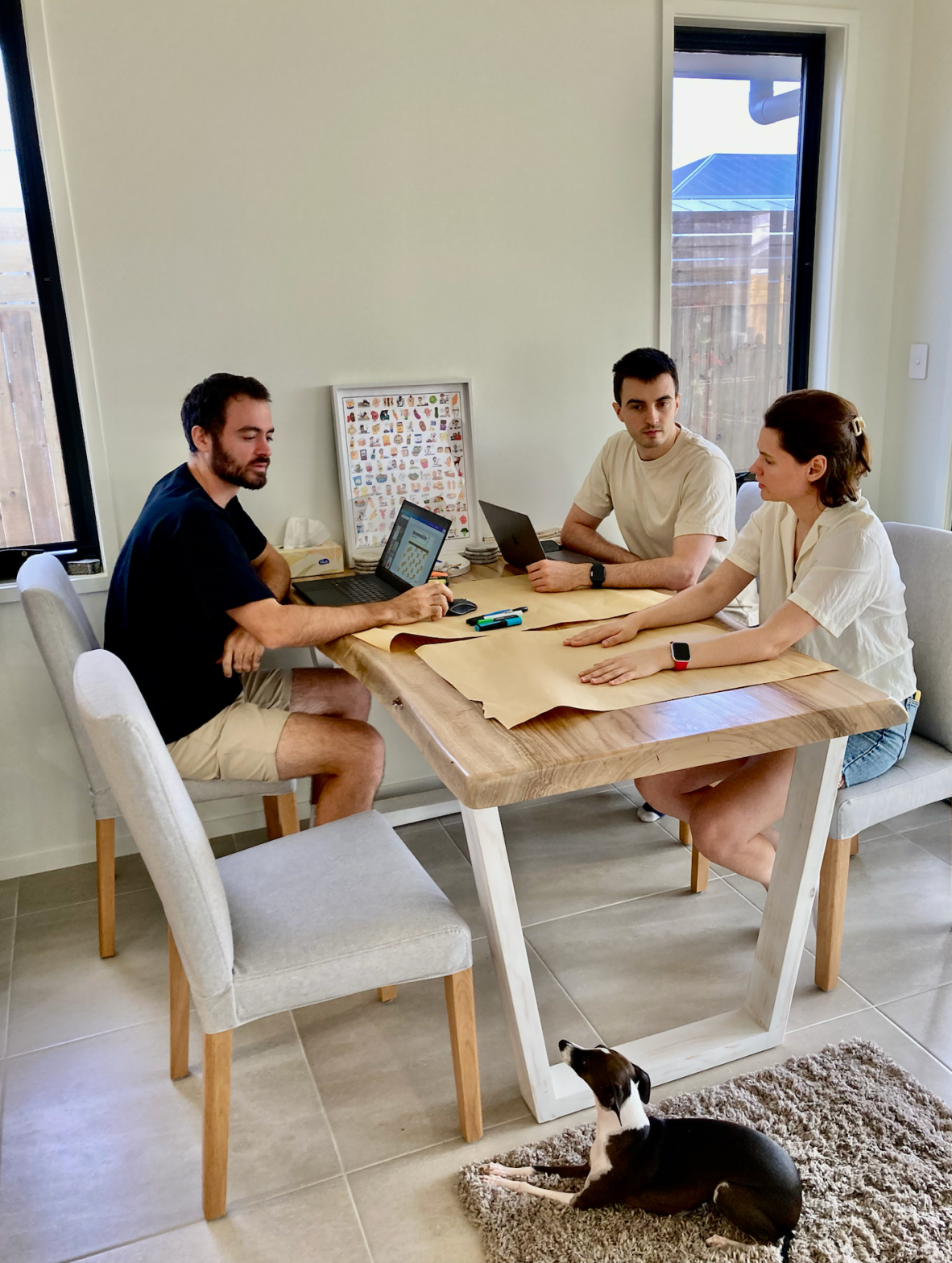 The Cooked game developers sitting around a light coloured table with laptops and large pieces of paper. 