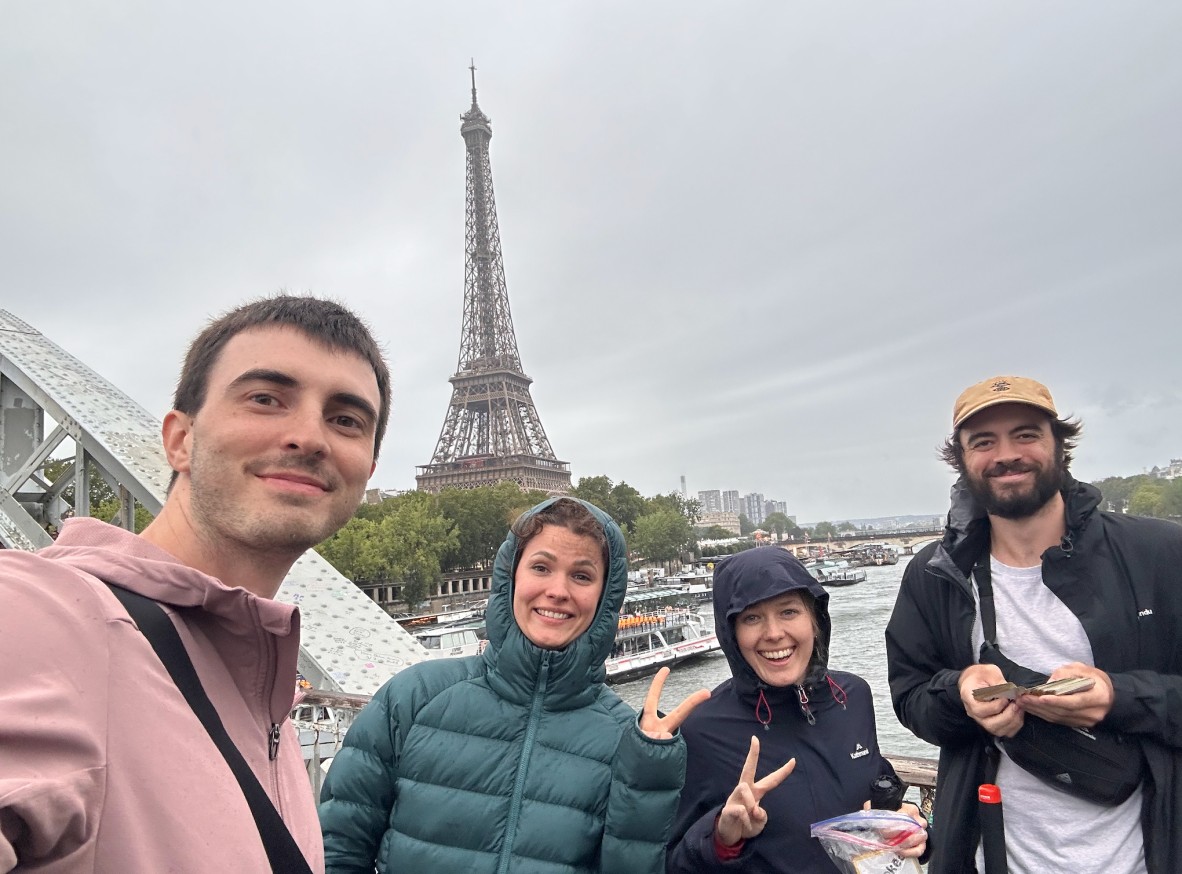 a group shot of four people (who developed the Cooked game) in front of the Eiffel tower in Paris. They are all smiling and seem happy, also all wearing jackets. 