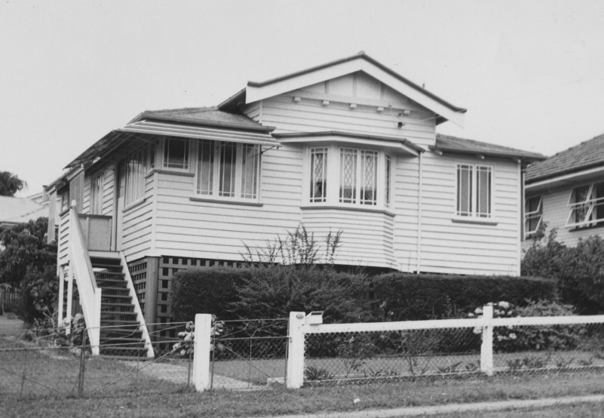 A multi gable house with a small fence, a hedge and a staircase at the side