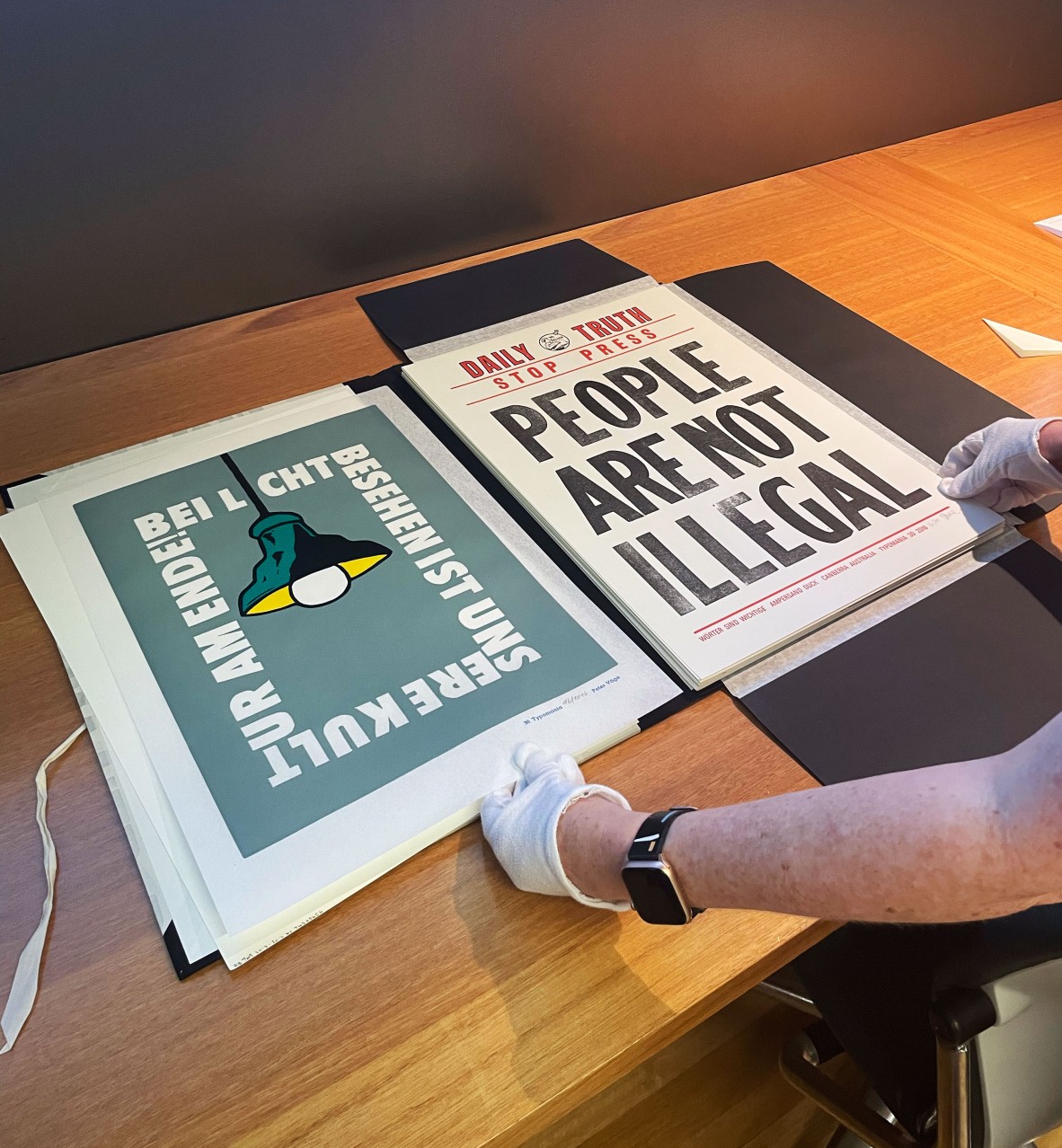 Two posters with someone reaching out holding them with white gloves. The pieces ae illustrated and contain a strong message.