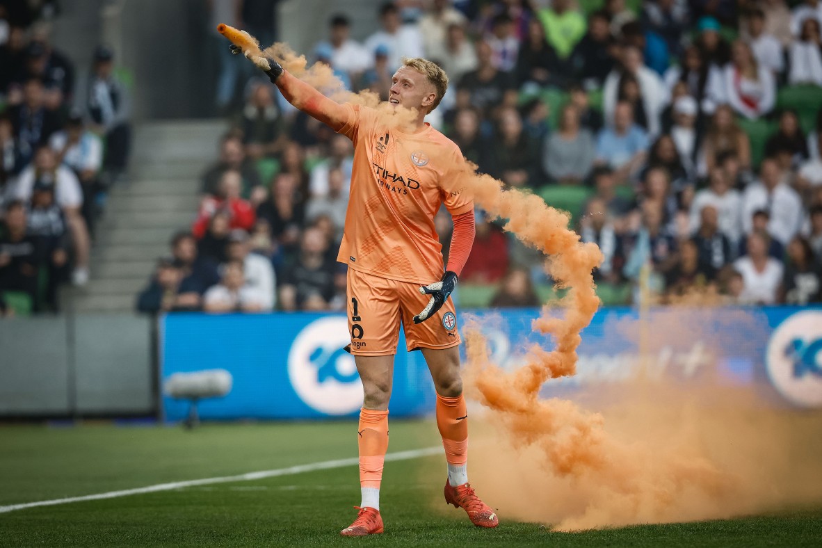 Photo of Melbourne City goalkeeper Tom Glover tries to remove a flare that was thrown onto the pitch