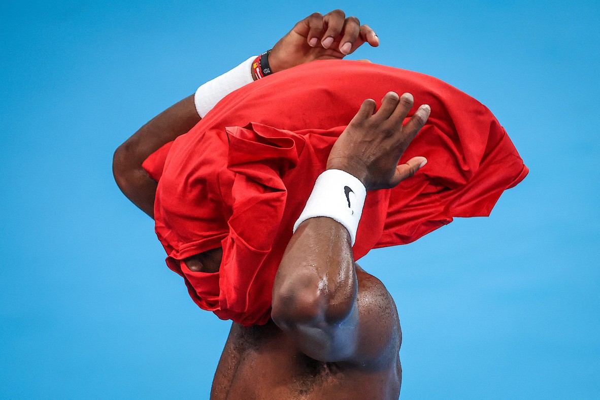 An action photo of a tennis player changing shirts, contrasting colours of blue and red