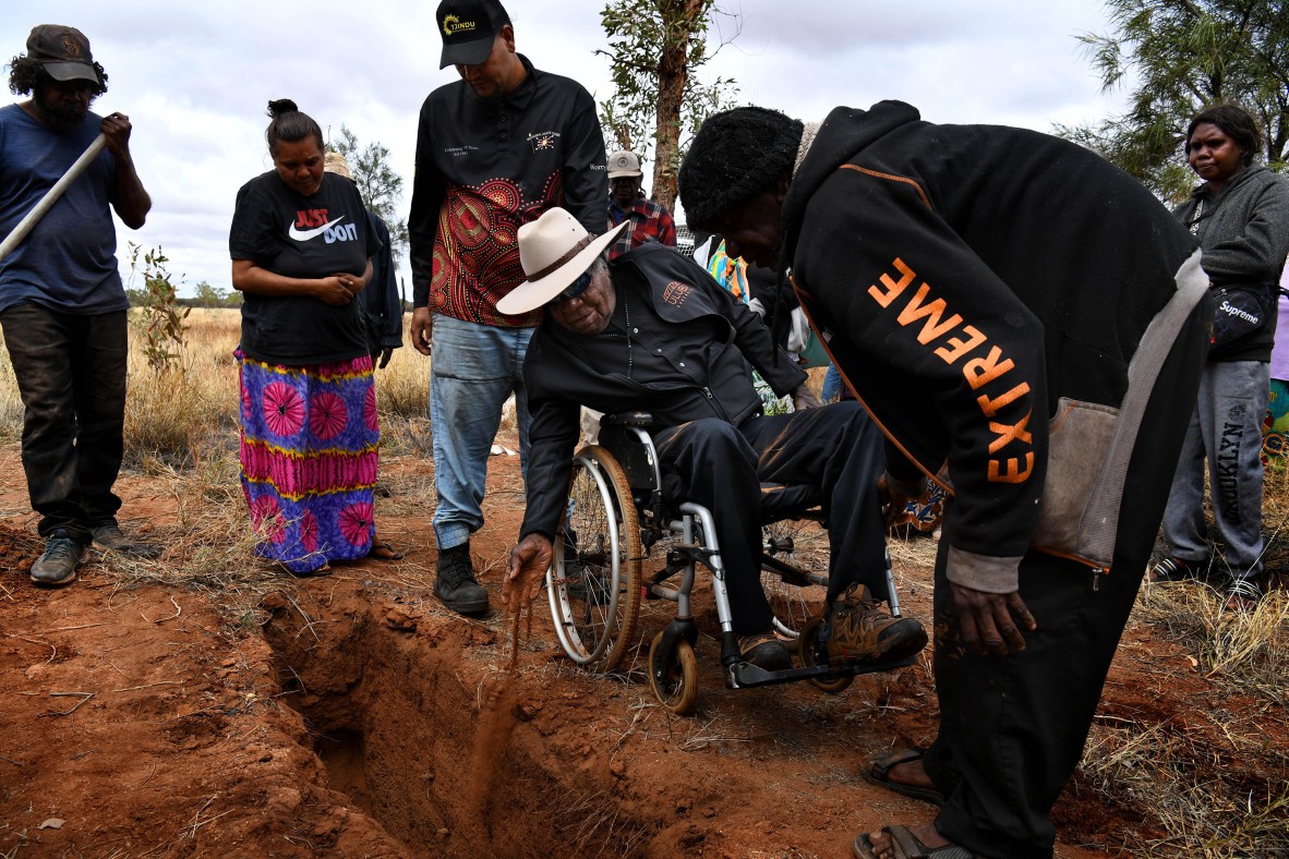 A photo of Uluru traditional owner Reggie Uluru dropping soil into Yukun's grave from his wheelchair
