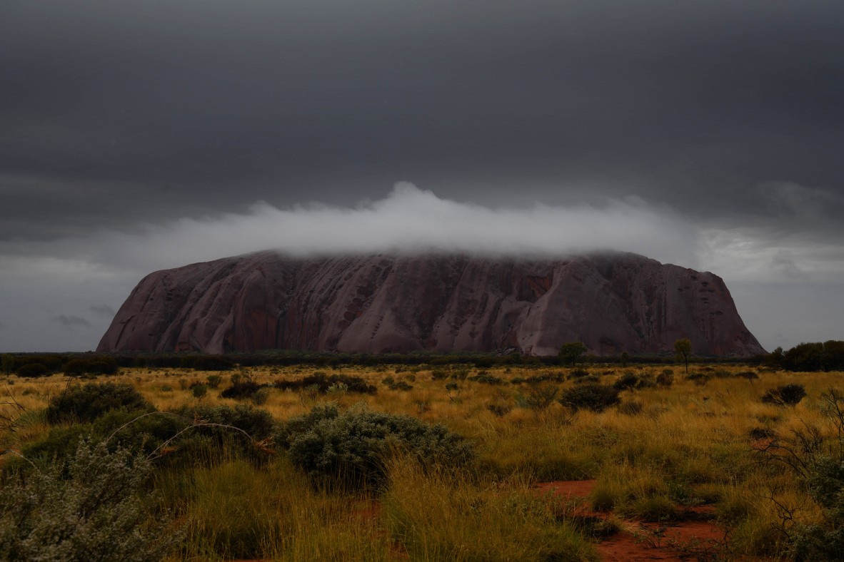 A photo of a sunrise over Uluru with clouds around the mountain