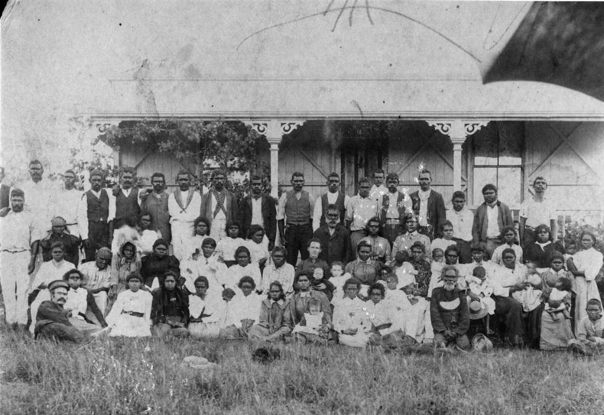 Large group of Aboriginal Australian men, women and children posing outside a house, Deebing Creek Mission, Queensland, ca. 1896-1897