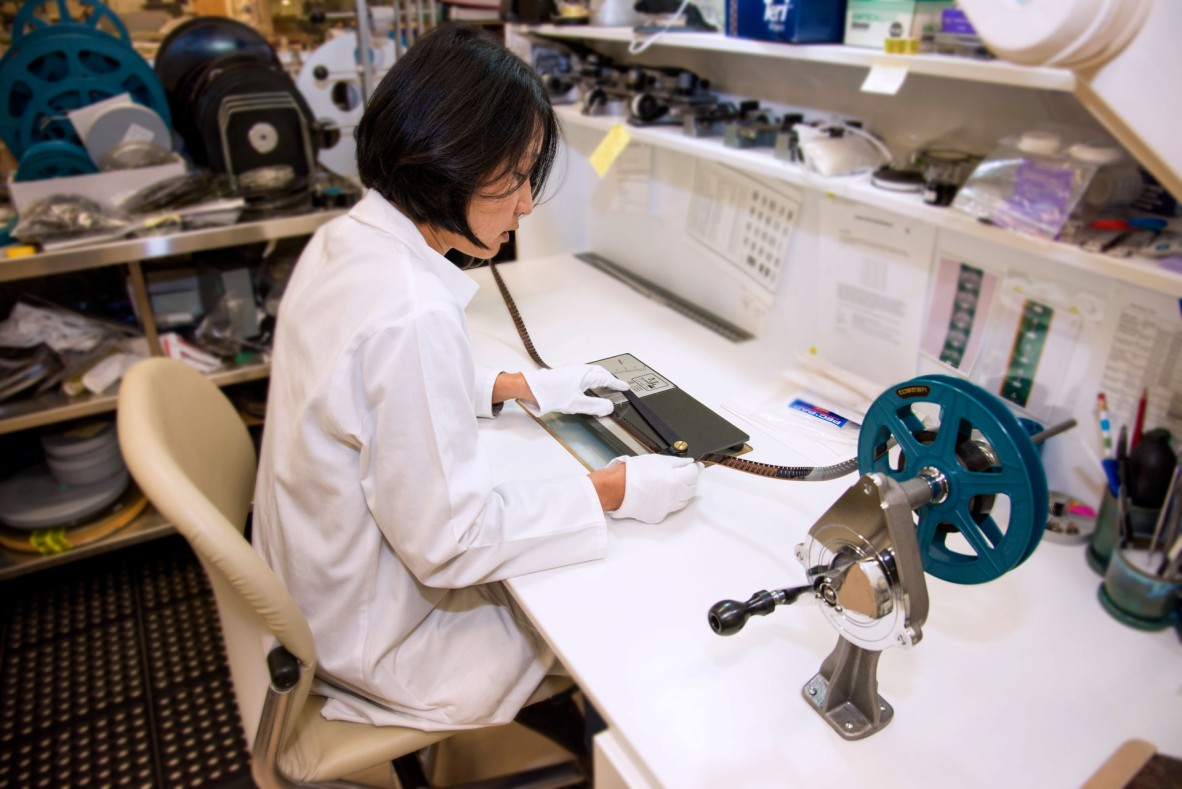 State Library staff member sitting at a desk and feeding old film into a reel.