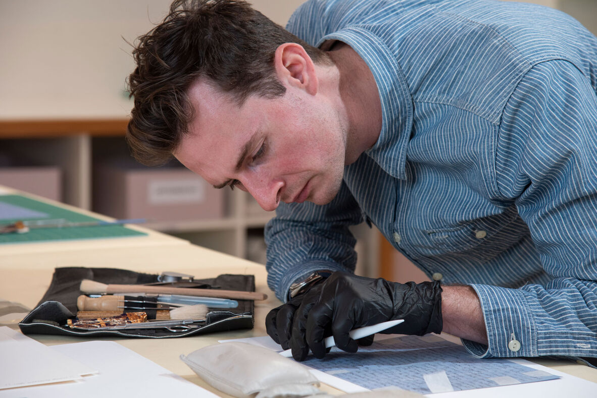 Man restoring old letter with conservation tools sitting on lab bench