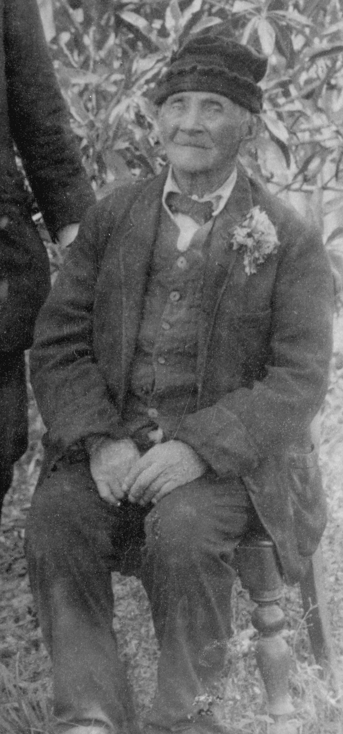 Portrait of elderly man in a suit wearing a knitted hat, sitting on a chair in the garden