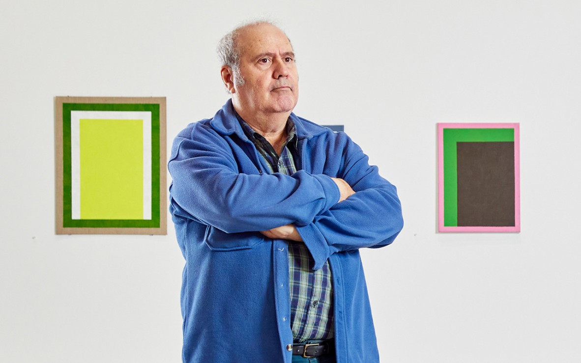 Man standing in front of abstract colour artworks with arms folded
