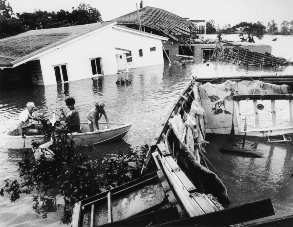 This image depicts the flotsam and jetsam of flood damage as people in a rowboat inspect submerged homes at Yeronga on the banks of the Brisbane River.