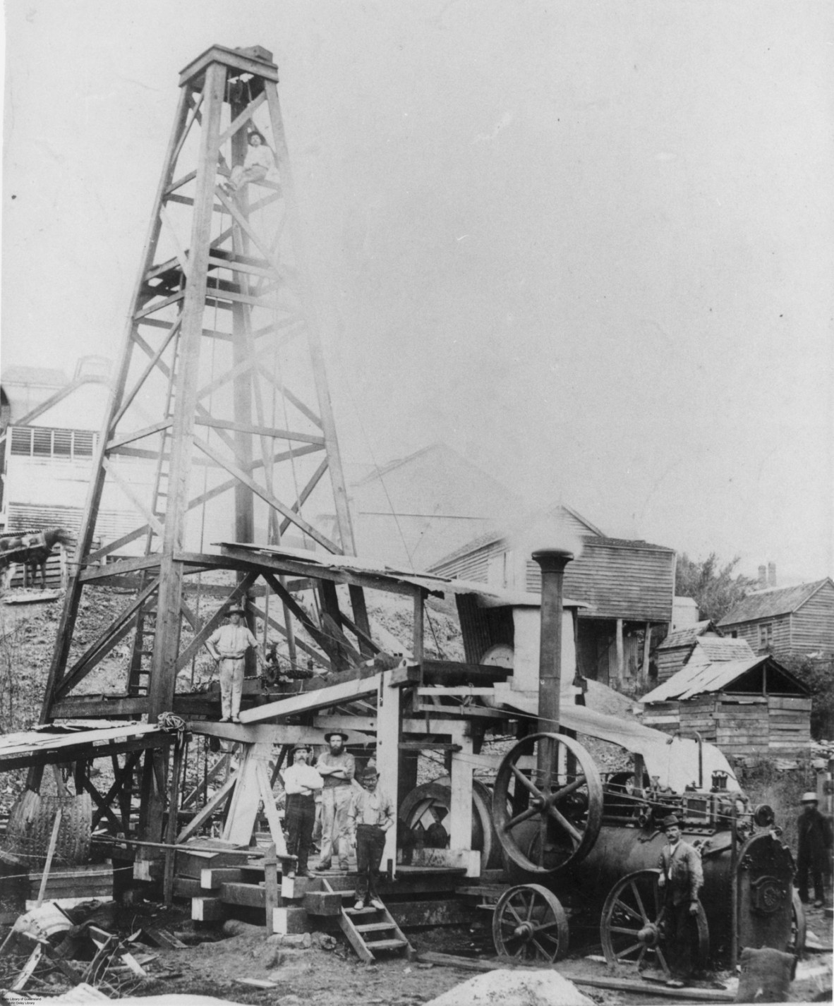 A black and white image shows a drilling plant at the Castlemaine Brewery in Brisbane, 1895. The portable engine is clearly visible. Workmen pose in front of the machinery. 'Altitude 617 ft. Depth 600 ft. Yield per 24 hours 3,000,000 gallons. Pressure per square inch 185 lb. Temperature 115 degrees Fah. Boring machinery bore abandoned' 
